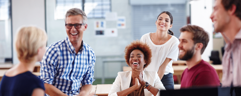 Group of coworkers sitting in office, laughing and smiling while discussing employee engagement software