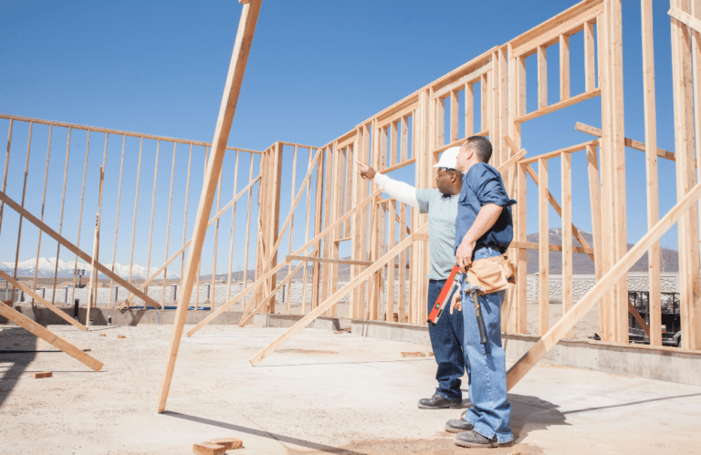 Two men on construction site, pointing at the wall framing on a house