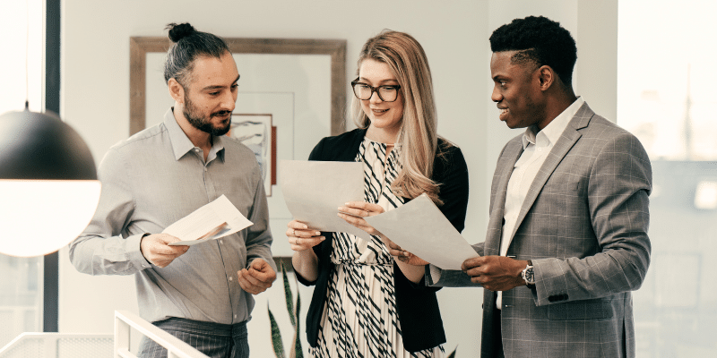 Three business professionals in an office reviewing documents together, engaged in discussion and analysis.